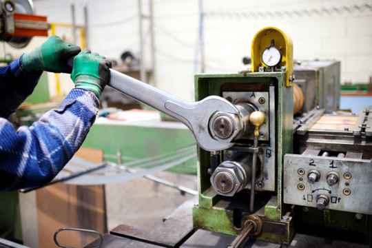 一个工厂维修工人用大扳手调整机器的形象。